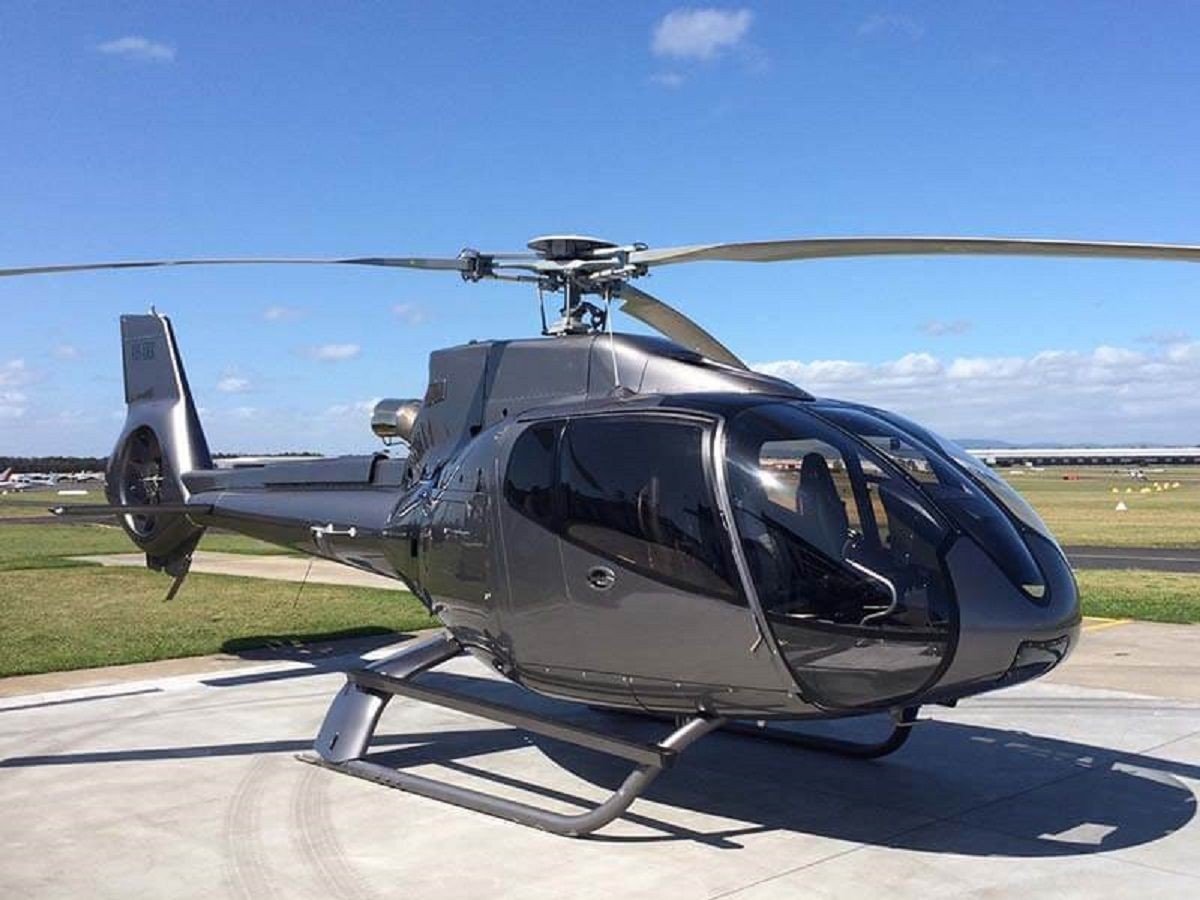 Sleek black helicopter parked on a tarmac with a clear blue sky in the background.