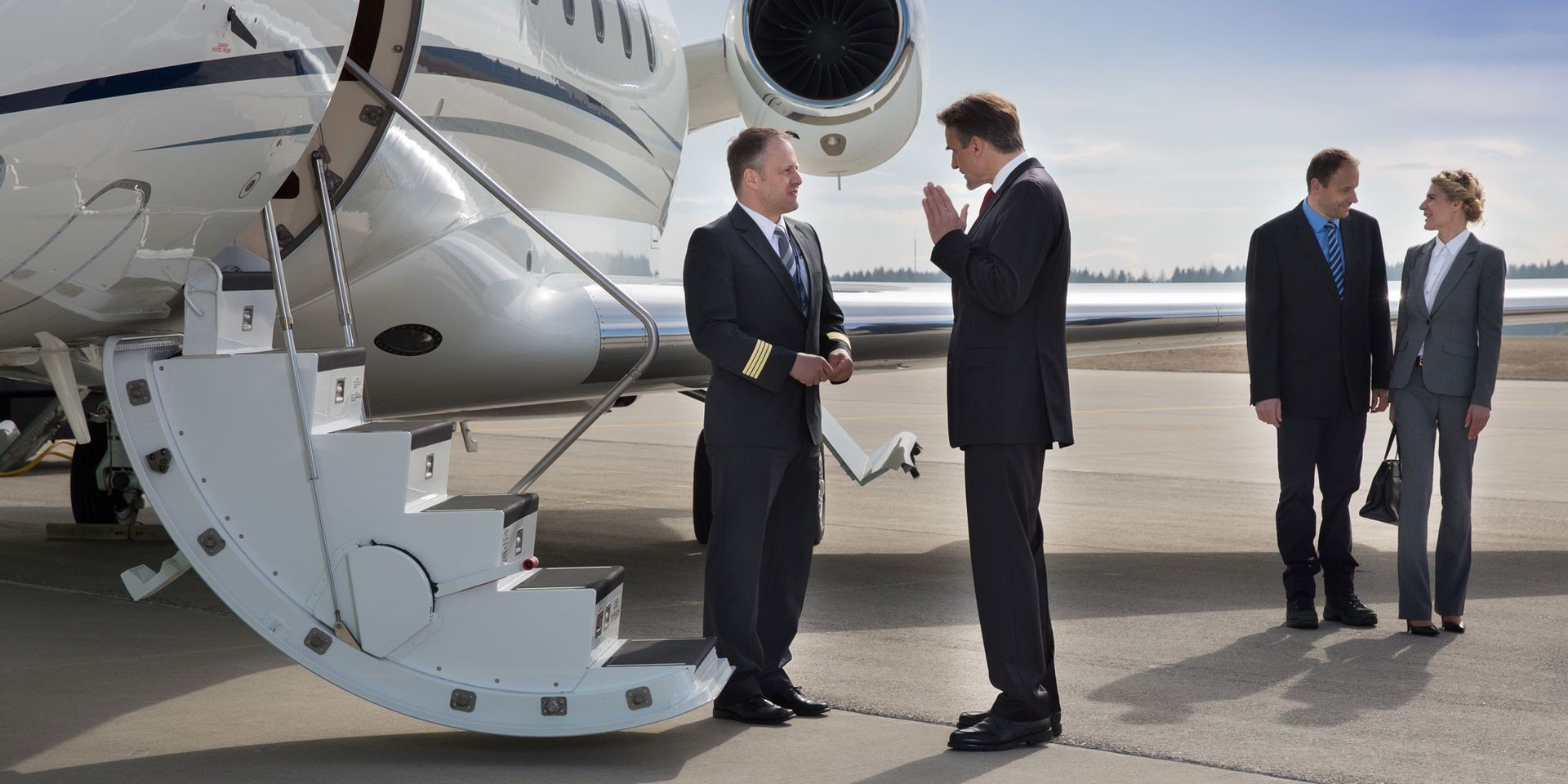 Business people conversing near a private jet on an airport tarmac.