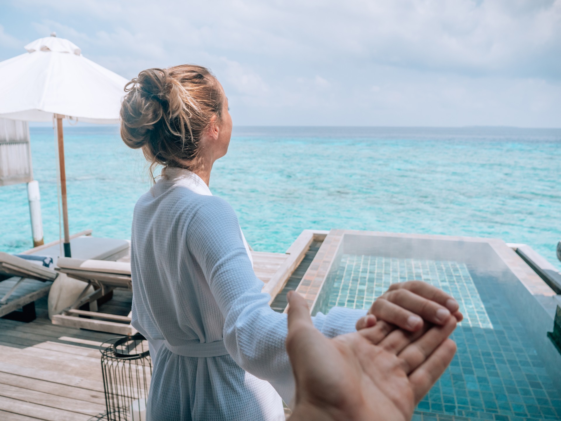 Couple holding hands in the Maldives, woman leads the way to outdoor patio